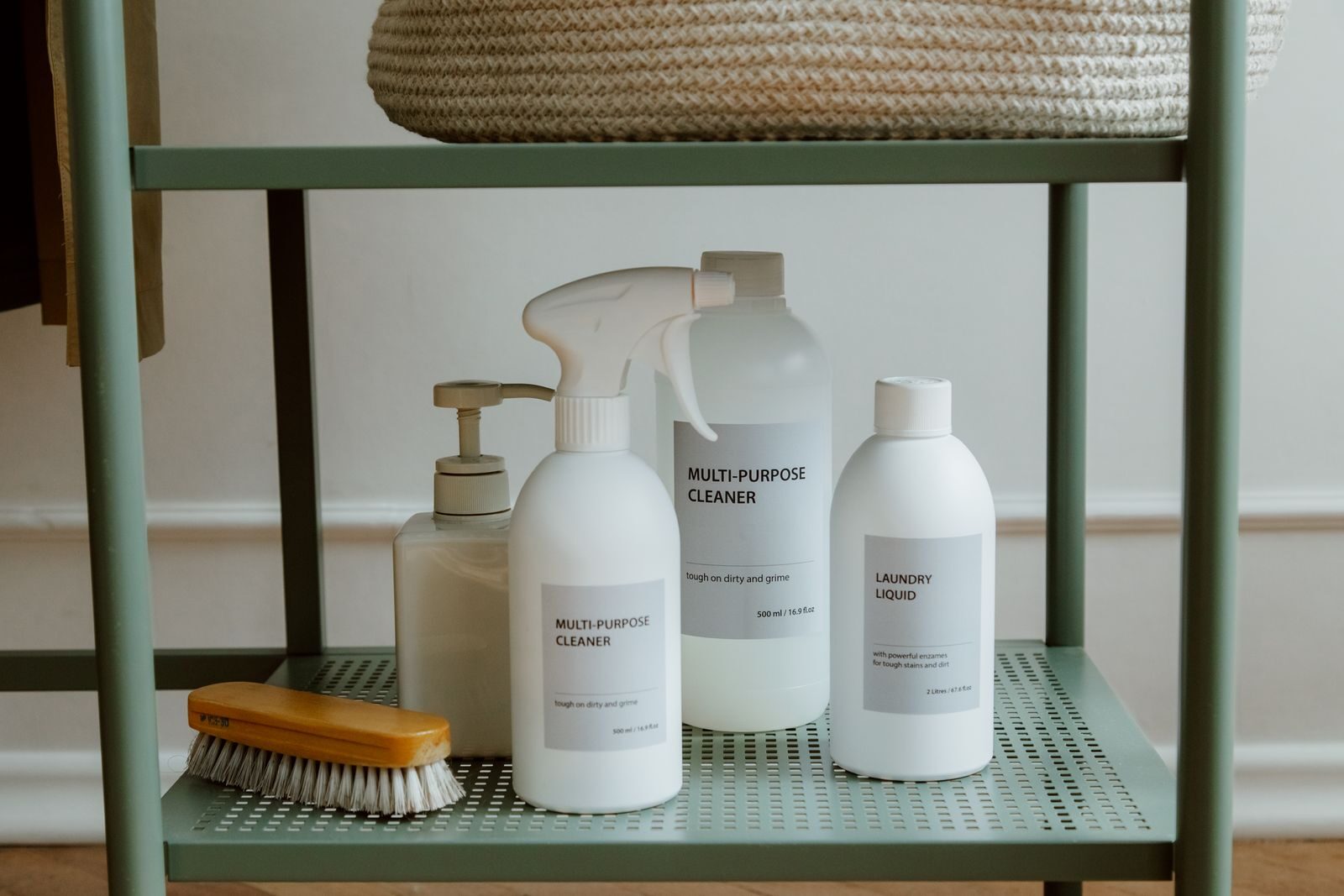 Natural cleaning products including spray bottle and liquid cleaners on a mint green shelf with wooden brush