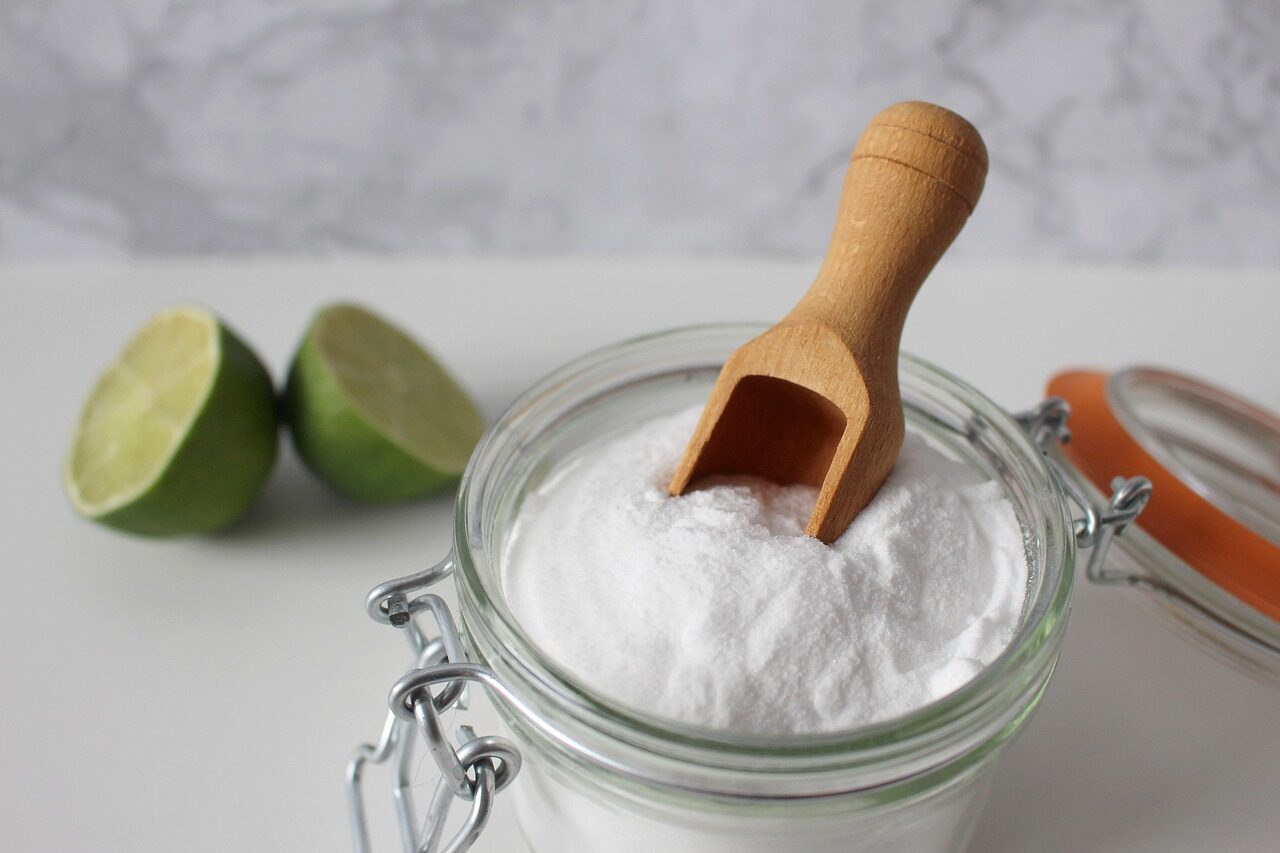 A jar of baking soda with a wooden scoop, one of the two staples people mix for cleaning