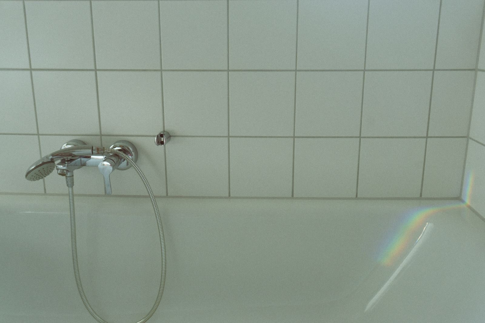 Mildew darkening the grout and sealant lines on white bathroom tiles
