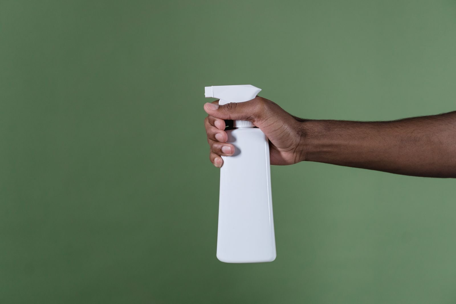 Hand holding a white spray bottle against a green background for natural cleaning applications