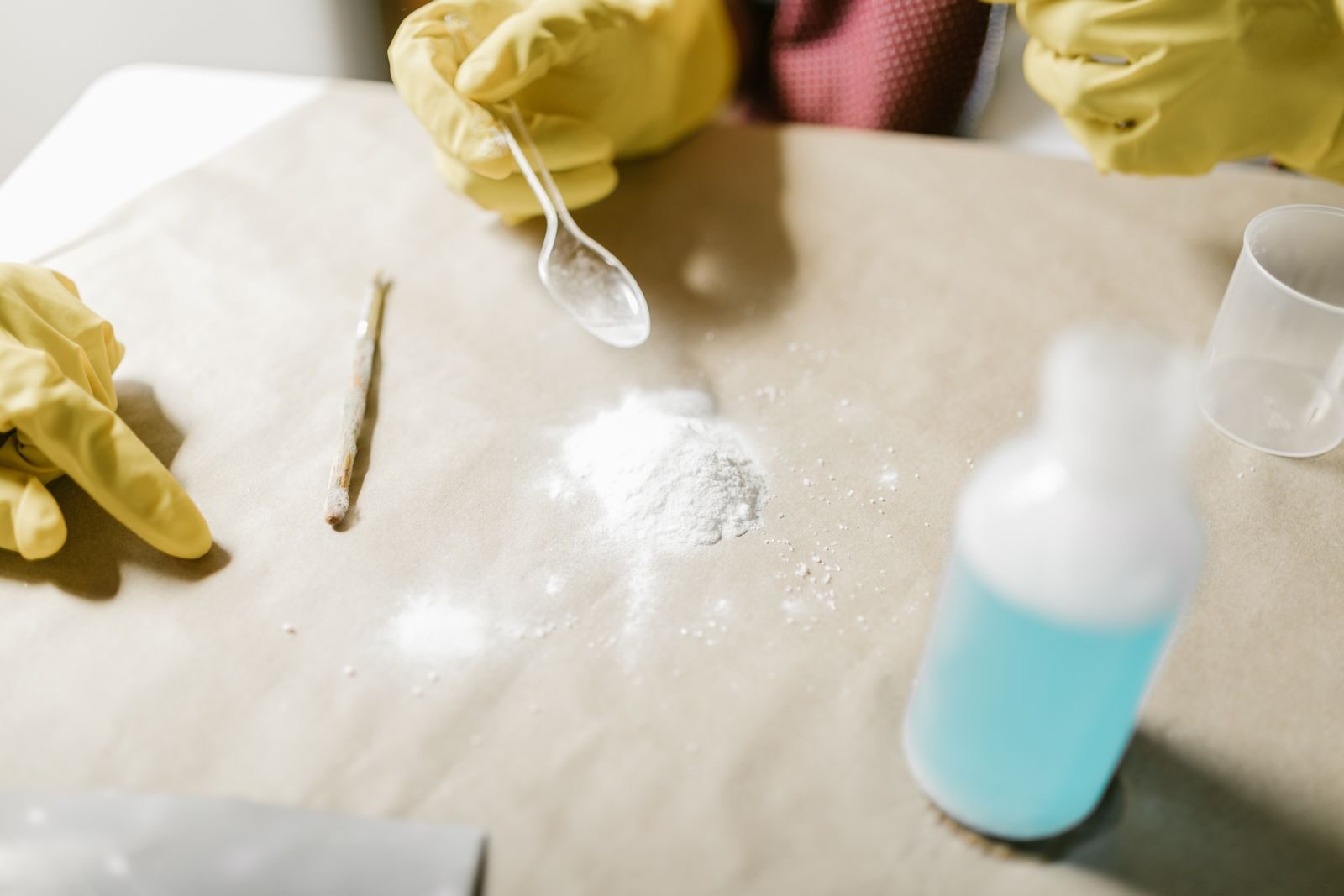 Gloved hands cleaning with baking soda and a spray bottle on a work surfaceImage title: Cleaning with baking soda and spray