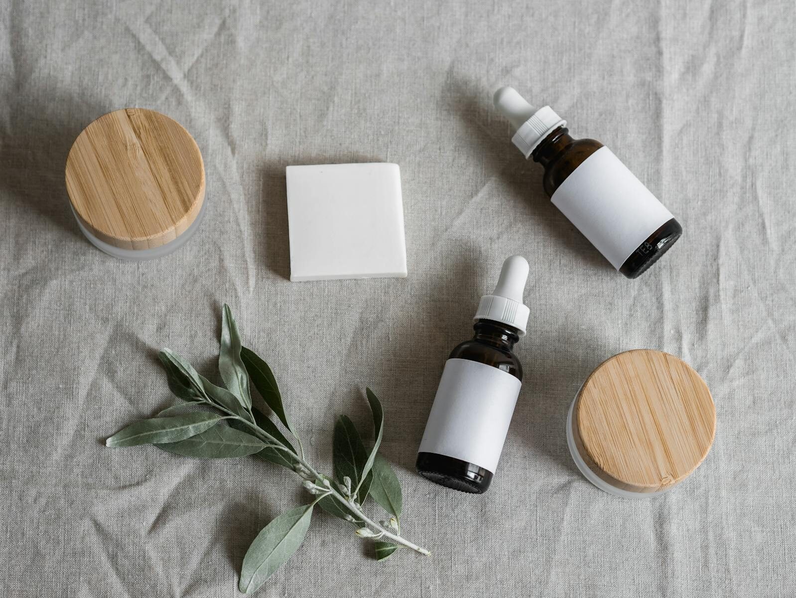 Natural skincare serums and cream jars with plant sprig on linen background