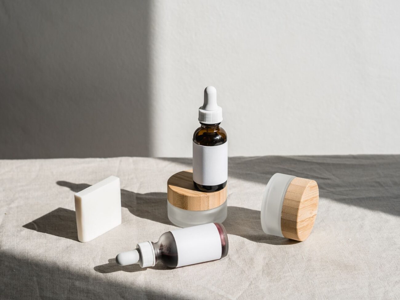 Natural skincare serum bottles and cream jar with bamboo lids on natural linen in daylight