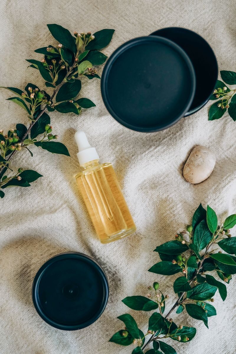 Golden plant oil serum dropper bottle with botanical sprigs and cream jars on natural linen