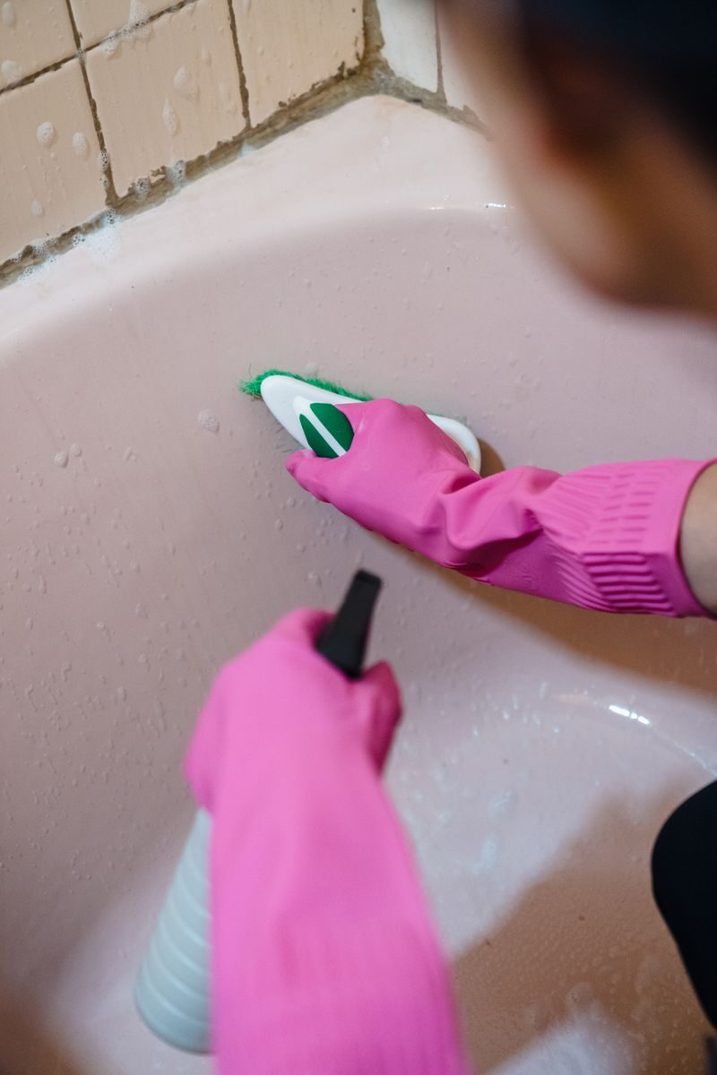 Gloved hands scrubbing mould from a bathroom with a brush and spray, the kind of cleaning that fails if the damp is not fixed