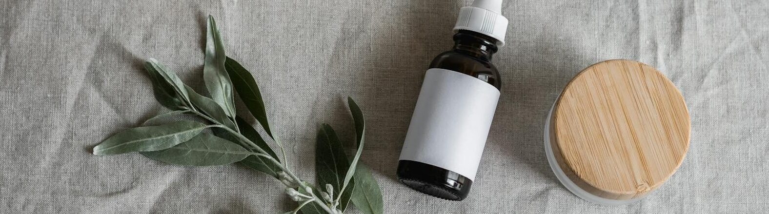 Natural skincare serums and cream jars with plant sprig on linen background