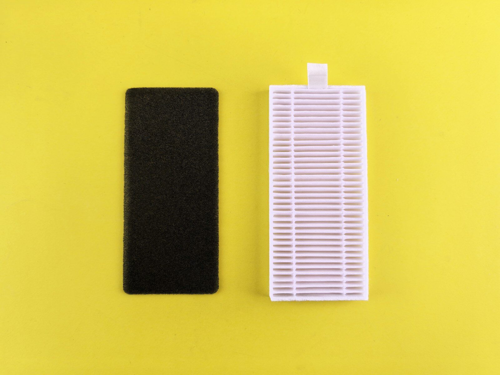 A black foam pre-filter beside a white pleated HEPA style filter showing folded media