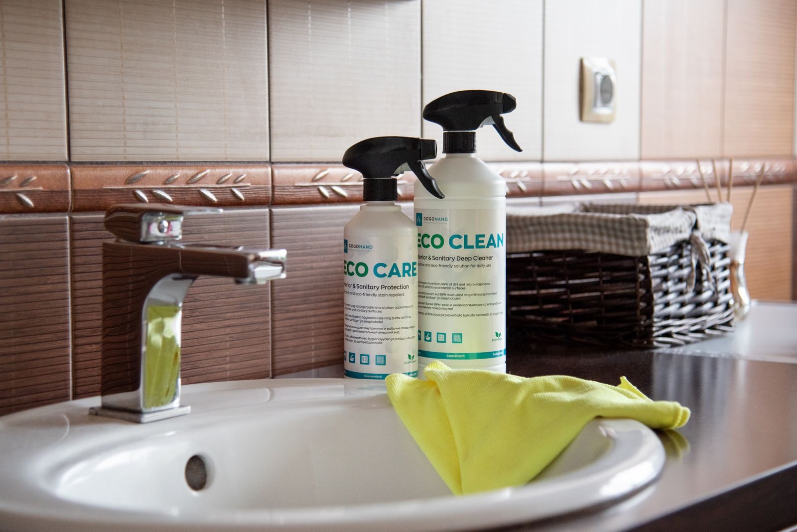 Two eco-labelled cleaning spray bottles on a bathroom sink, showing green claims and small certification-style icons