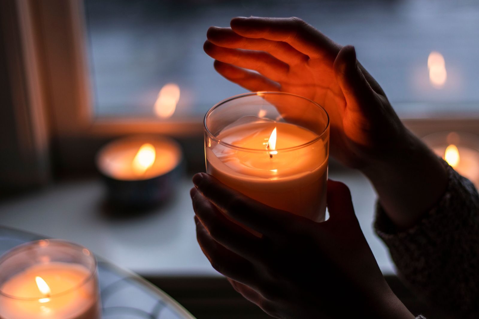 Hands warming near a lit candle in a cosy room