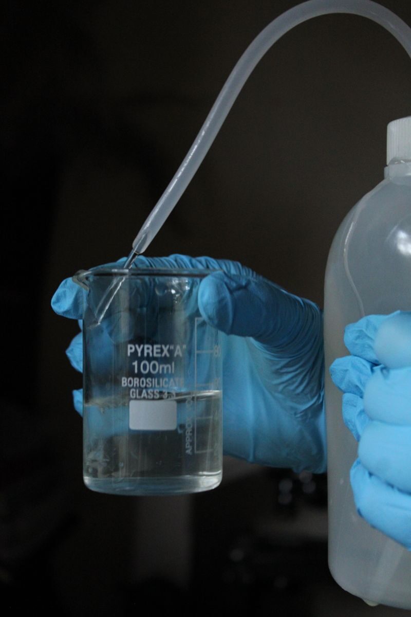 Measuring solution concentration Gloved hands measuring a clear solution in a beaker in a lab setting
