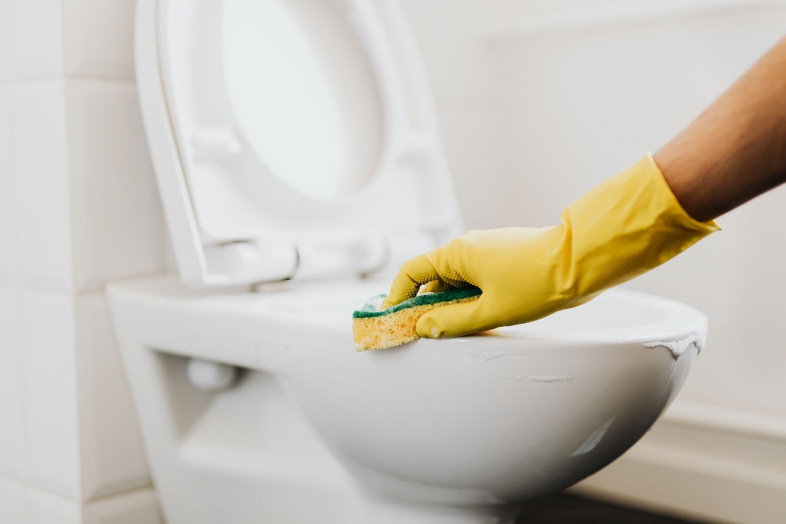 A gloved hand cleaning a white toilet bowl in a bathroom, a surface where hydrogen peroxide works well