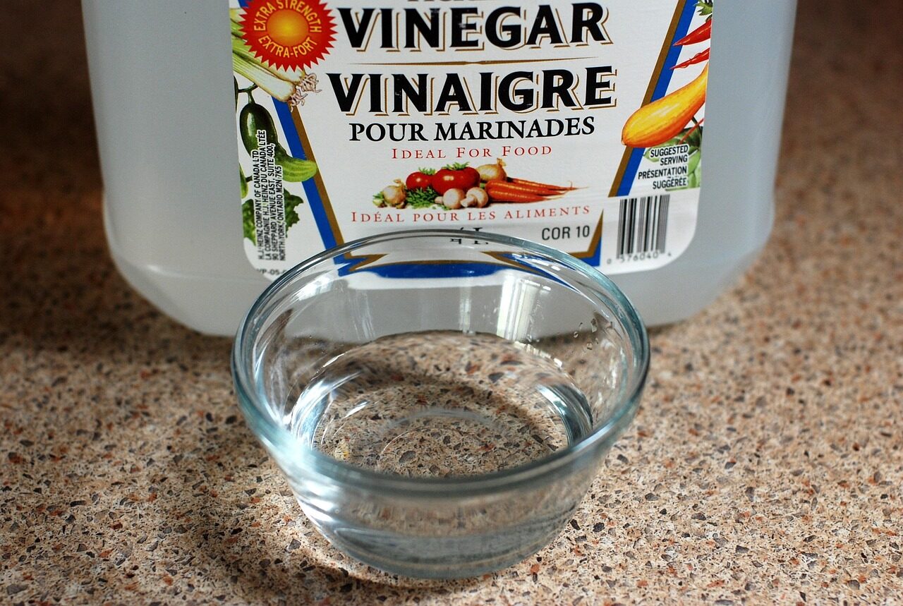 A jug of white vinegar beside a small glass bowl of vinegar on a kitchen counter