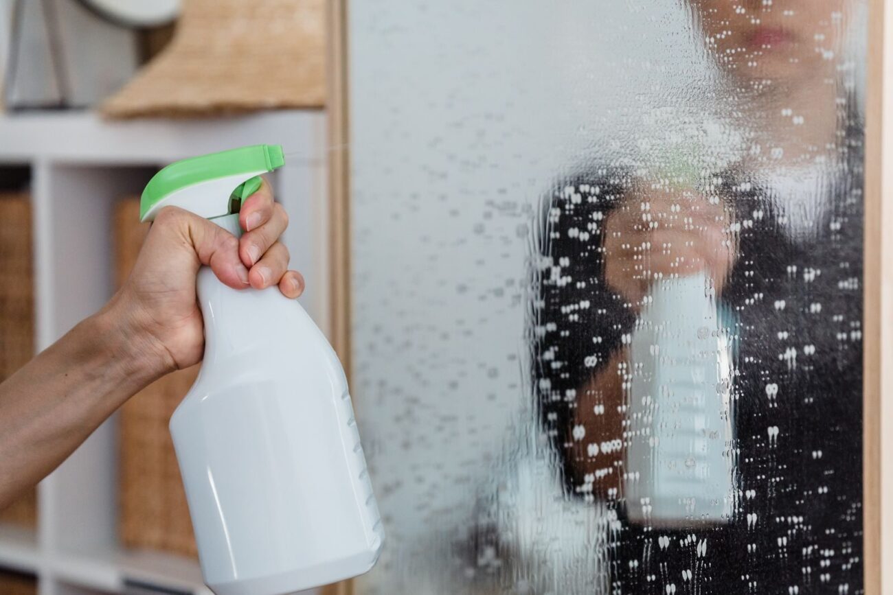 A hand spraying a plant-based cleaning product onto a glass surface