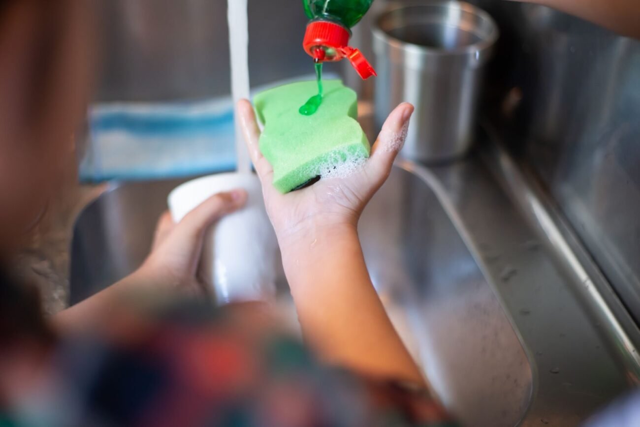 Dish soap being squeezed onto a sponge over a kitchen sink, the everyday use people ask about